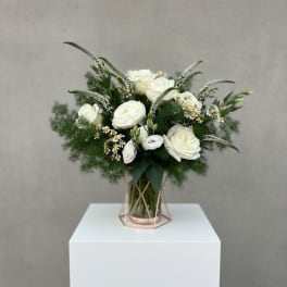 White roses and small daisies in a glass vase with greenery