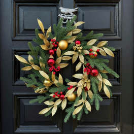 Christmas wreath with gold leaves, red berries, and ornaments on a black door