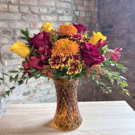 Mixed bouquet of roses, marigolds, and alstroemeria in an amber glass vase