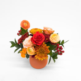 Orange and red mixed flower arrangement in a round orange vase