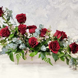 Low rectangular centerpiece of red roses with pink blossoms and eucalyptus in a wooden box
