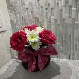 Pink roses and white daisies in a black vase with a plaid bow
