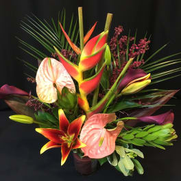 Tropical bouquet with anthuriums, lilies, and palm fronds in a vase