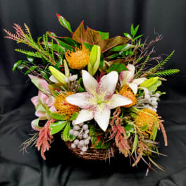 Tropical flower arrangement with white lilies and orange pincushion blooms in a basket.