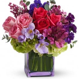 Mixed bouquet of roses, hydrangeas, and purple flowers in a purple glass vase