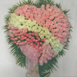 Heart-shaped floral arrangement of pink and white roses with a pink ribbon