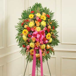 Standing floral spray with bright mixed flowers and a pink ribbon on an easel