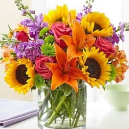 Bouquet of sunflowers, orange lilies, pink roses, and purple flowers in a glass vase