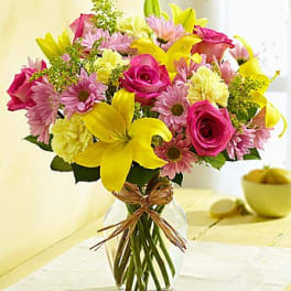 Bouquet of pink roses, yellow lilies, and pink daisies in a glass vase