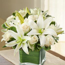White lilies and roses arranged in a square glass vase