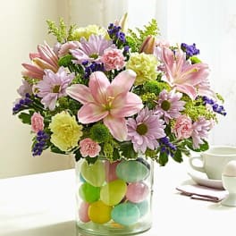 Pink lilies and daisies in a glass vase with colorful eggs