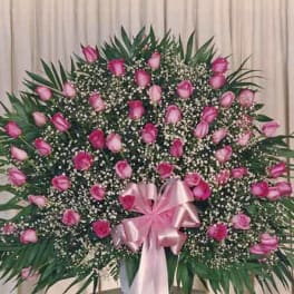 Large standing spray of pink roses with a pink ribbon bow