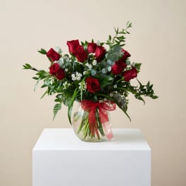 Red roses arranged in a clear glass vase with a red ribbon