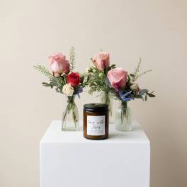 Three small rose arrangements in glass vases with a candle in front