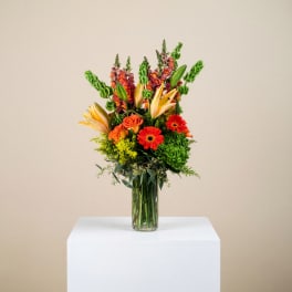 Tall mixed bouquet in a clear glass vase with orange, red, yellow, and green flowers