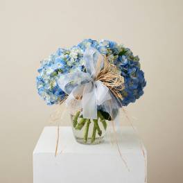 Blue hydrangea bouquet in a clear glass vase with a sheer ribbon bow
