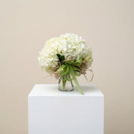White hydrangea bouquet in a small glass vase with a green ribbon
