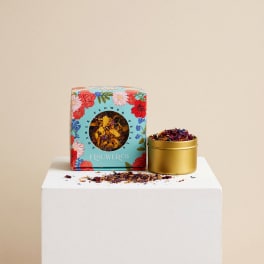 Floral tea in a decorated box beside a gold tin on a white pedestal