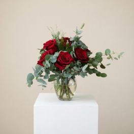 Red roses in a clear glass vase with eucalyptus