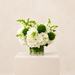 White floral arrangement in a clear glass vase with green accents
