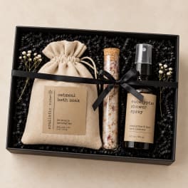 Gift box with bath soak, spray bottle, and dried flowers tied with a black ribbon