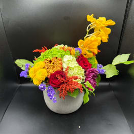 Colorful mixed flower arrangement in a gray vase with yellow orchids and red roses