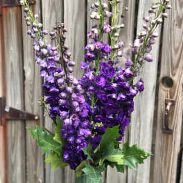 Tall purple flower arrangement in a green vase with leafy accents