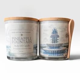 Two glass candles with wooden lids and pineapple fountain labels