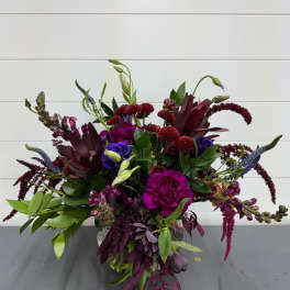 Mixed bouquet of burgundy, purple, and blue flowers in a clear vase