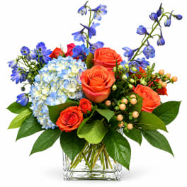 Bouquet of orange roses, blue hydrangea, and blue flowers in a glass vase