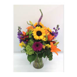 Colorful mixed bouquet in a clear glass vase with sunflowers and lilies