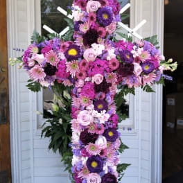 Tall cross-shaped standing spray of pink and purple flowers on a metal stand.