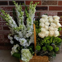 Tall white snapdragons and roses arranged with green accents in a woven basket