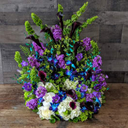 Tall one-sided arrangement with purple blooms, blue orchids, dark calla lilies, and white hydrangeas