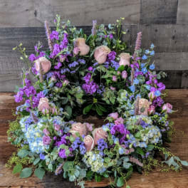Pastel wreath of pink roses and purple and blue blooms arranged in a ring.