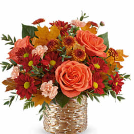 Orange roses and red daisies in a woven basket with autumn leaves