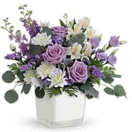 Lavender roses and white flowers in a clear square vase