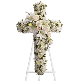 White floral cross arrangement on a stand with lilies and roses