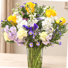 Mixed bouquet of yellow, white, purple, and lavender flowers in a glass vase