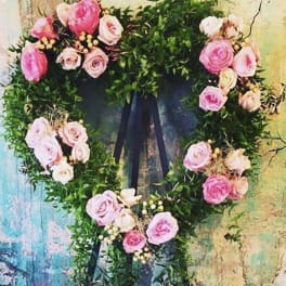 Heart-shaped floral wreath with pink roses and greenery on a dark ribbon