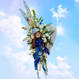 Floral tribute with a teddy bear and blue ribbon against a sky background