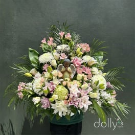 Large pastel floral arrangement with an angel figurine in a green container