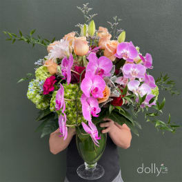 Large bouquet of pink orchids, peach roses, and green hydrangeas in a glass vase