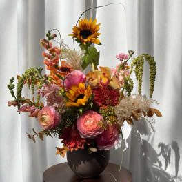 Mixed bouquet in a dark vase with sunflowers, pink blooms, and orange flowers