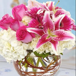 Pink roses and lilies arranged with white hydrangeas in a glass vase