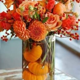 Orange floral arrangement in a clear glass vase with small pumpkins inside