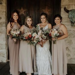 Bride and three bridesmaids holding mixed bouquets in front of a rustic doorway