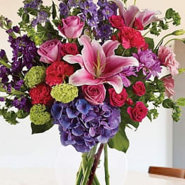 Mixed bouquet of pink roses, lilies, and purple flowers in a clear vase