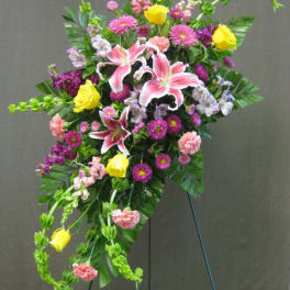Standing floral spray with pink lilies, yellow roses, and purple blooms