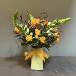 Orange roses in a pale vase with a yellow ribbon